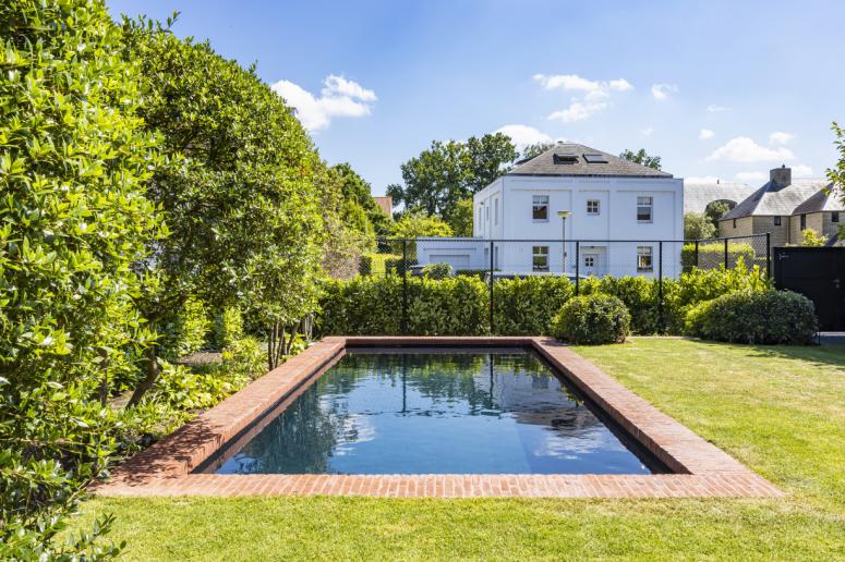 Zwembad in tuin met rode boordsteen met zicht op een wit huis